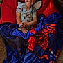 child, boy, smiling, blanket, spiderman, red_chair, carpet, toy, bowl, dog_food, indoor, happy, cute, person, clothing, short_sleeve, hair, face, sitting, home