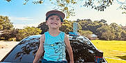 Ashtyn joined the competition — help win amazing prizes! child, boy, smiling, cap, tank_top, shorts, car, honda, trunk, outdoor, sunny, tree, leafy, grass, water_bottle, sidewalk, residential, happy, summer, playful