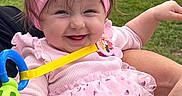 Maria Seraya is registered to the contest to win money with this photo: baby, girl, smiling, pink_bow, headband, pink_dress, heart_pattern, outdoor, grass, toy, hand, car, sidewalk, joyful, cute, child, person, holding, happy, infant