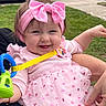 baby, girl, smiling, pink_bow, headband, pink_dress, heart_pattern, outdoor, grass, toy, hand, car, sidewalk, joyful, cute, child, person, holding, happy, infant