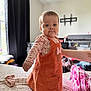 baby, child, orange_dress, minnie_mouse, bed, bedroom, curtains, window, person, arm, clothing, standing, indoor, furniture, television_mount, blanket, support, casual, cute, young