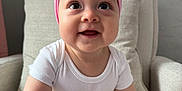 Adalyn is registered to the contest to win money with this photo: baby, child, pink_bow, headband, white_onesie, beige_pants, armchair, cushion, indoor, smiling, curious, sitting, cute, happy, infant, person, skin, face, hand, foot