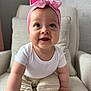 baby, child, pink_bow, headband, white_onesie, beige_pants, armchair, cushion, indoor, smiling, curious, sitting, cute, happy, infant, person, skin, face, hand, foot
