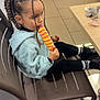 black_leggings, black_shoes, blue_sweater, braided_hair, brown_chair, chair, child, cute, eating, floor_tiles, girl, hair_accessory, indoor, pacifier, popsicle, sitting, striped_popsicle, striped_socks, stuffed_toy, table