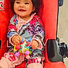 baby, child, stroller, toy, flower_headband, curly_hair, smiling, red, colorful, clothing, happy, indoor, cute, portrait, sitting, infant, playful, person, accessory, bright