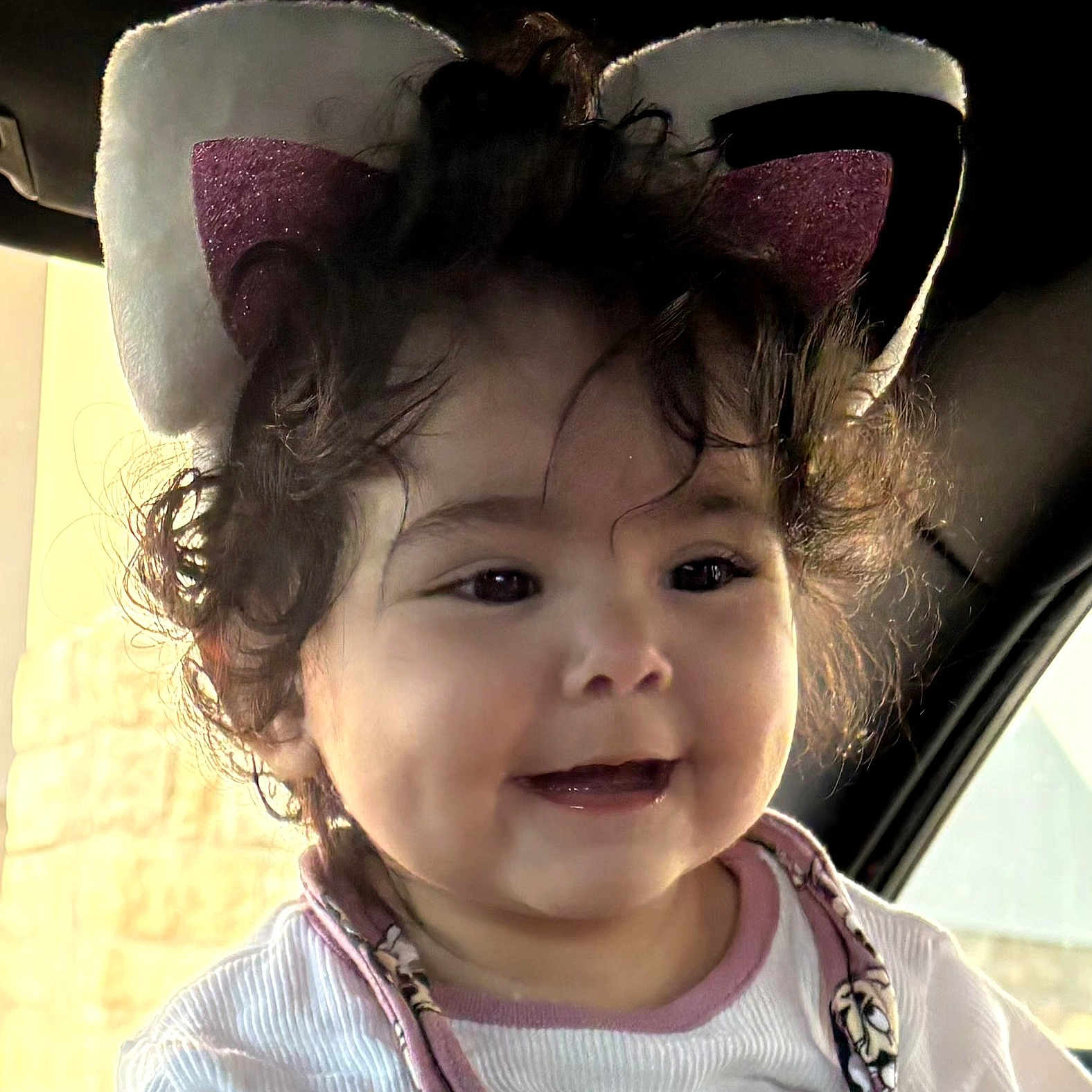 Ariela is registered to the contest to win money with this photo: baby, child, face, smile, curly_hair, headband, cat_ears, indoors, car, seat, clothing, cute, happy, portrait, infant, person, toddler, apparel, young_child, expression