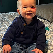 Bryson joined the competition — help win amazing prizes! baby, child, infant, smiling, happy, portrait, sitting, bed, bedspread, bedroom, clothing, navy_outfit, jeans, pacifier, rosy_cheeks, blond_hair, face, hands, bare_feet, indoor