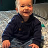 baby, child, infant, smiling, happy, portrait, sitting, bed, bedspread, bedroom, clothing, navy_outfit, jeans, pacifier, rosy_cheeks, blond_hair, face, hands, bare_feet, indoor