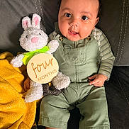 Jalen is registered to the contest to win money with this photo: baby, child, plush_toy, bunny, green_overalls, yellow_blanket, couch, smiling, portrait, indoor, cute, infant, socks, person, milestone, four_months, soft_toy, happy, seated, face