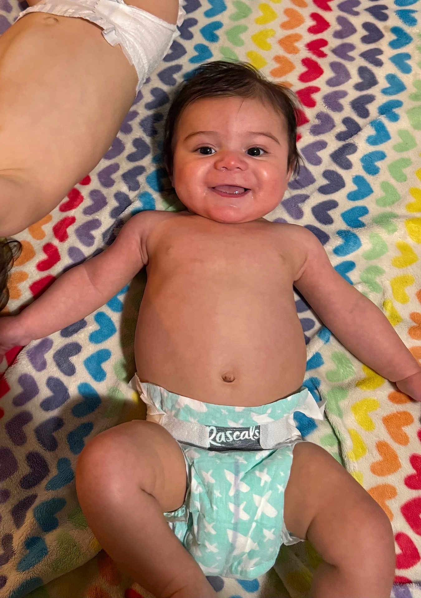 Niko is registered to the contest to win money with this photo: baby, diaper, smile, happy, infant, colorful_blanket, heart_pattern, lying_down, cute, child, skin, face, arm, leg, toddler, playful, two_children, indoors, closeup, expression