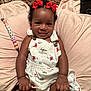 baby, child, smiling, red_bows, floral_dress, overalls, cushion, blanket, pacifier_clip, beads, indoor, carpet, cute, happy, portrait, infant, clothing, skin, person, lying_down