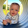 Côme a rejoint le concours — aidez-le/la à gagner de superbes lots ! toddler, child, baby, playground, tunnel, blue_eyes, outdoor, sunny, curious, smiling, long_sleeve_shirt, construction_vehicle_pattern, grass, daylight, cute, portrait, happy, face, head, hands