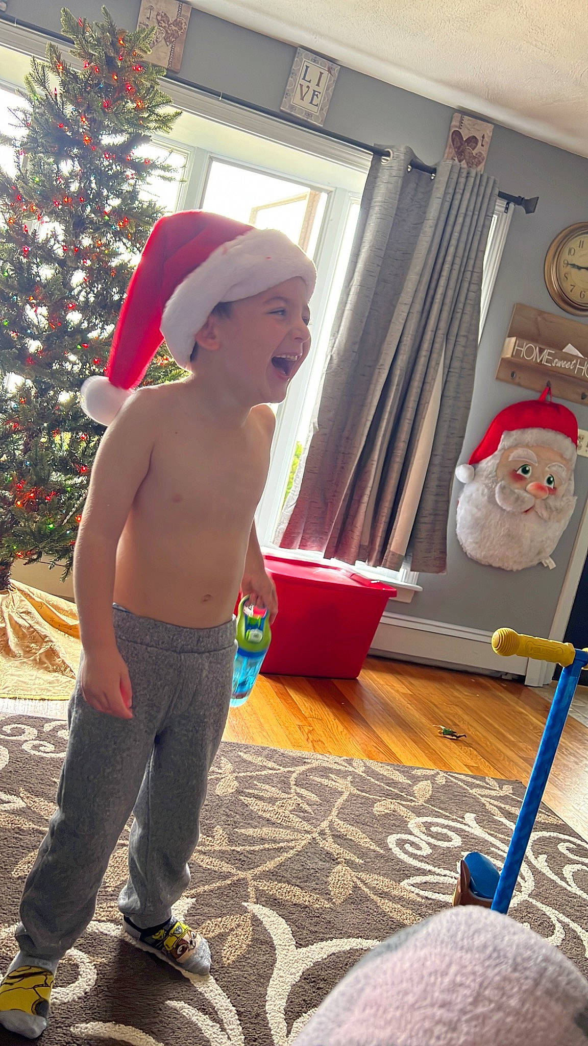 Cameron is registered to the contest to win money with this photo: abdomen, cap, child, christmas, christmas_tree, curtain, event, flooring, fun, happy, headwear, holiday, human_leg, leisure, party_supply, person, play, room, standing, toddler