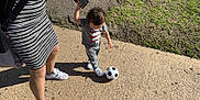 Ambrose is registered to the contest to win money with this photo: adult, casual_clothing, child, curly_hair, footwear, grass, holding_hands, outdoor, park, pavement, person, playing, shadow, sidewalk, soccer_ball, striped_dress, sunlight, sunny_day, walking, white_sneakers