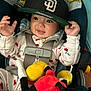 baby, child, car_seat, cap, hat, plush_toy, smile, happy, infant, clothing, straps, seatbelt, indoor, cute, playful, person, headwear, toy, hands, face