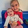child, baby, sibling, glasses, smile, happy, indoor, red_jacket, pink_pants, blue_bench, holding, cute, joyful, face, person, portrait, casual_clothing, infant, toddler, family