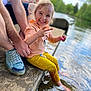 child, smiling, water, sitting, adult, hand, shoe, concrete, outdoor, nature, lake, footwear, casual_clothing, yellow_pants, pink_sweater, person, playful, happy, daylight, reflection