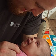 Sheïna a rejoint le concours — aidez-le/la à gagner de superbes lots ! baby, man, smile, indoor, play_mat, pink_clothing, beard, face, head, person, holding, joy, love, family, child, interaction, floor, wooden_floor, candid, affection