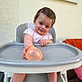 Livia a rejoint le concours — aidez-le/la à gagner de superbes lots ! baby_clothes, chair, child, cute, foot, hand, happy, high_chair, indoor, orange, person, pink_hair_clip, plastic, playful, short_hair, skin, smiling, toddler, wall, water_balloon