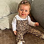 baby, casual, child, clothing, couch, cute, face, hair_clips, happy, home, indoor, leopard_print, overalls, person, pillows, sitting, smiling, toddler, white_socks, young_child