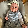 baby, child, girl, smile, headband, polka_dot, dress, floral_pattern, high_chair, indoor, person, hand, face, long_sleeve, seated, cute, happy, skin, wooden_door, tile_floor