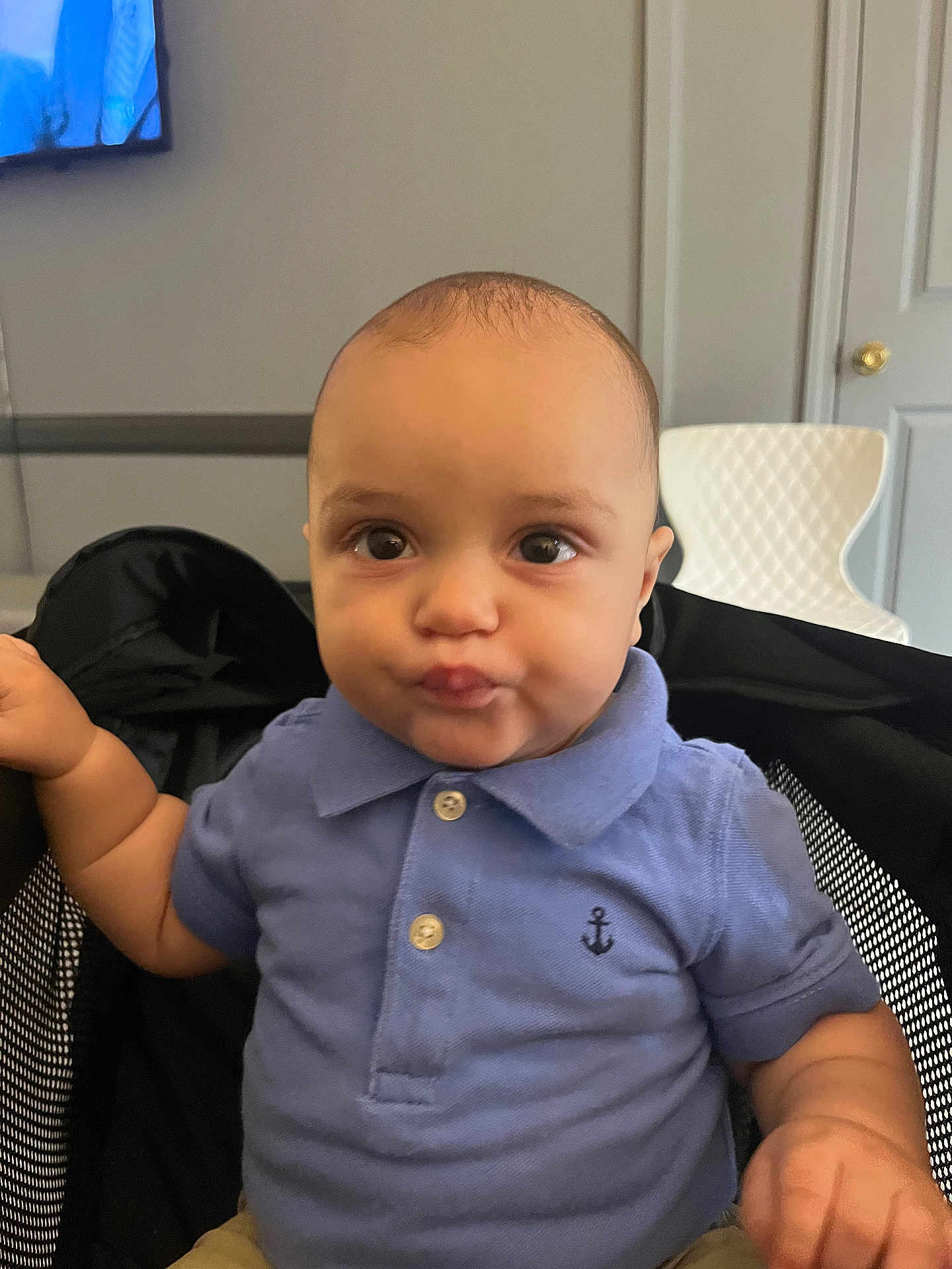 Joel is registered to the contest to win money with this photo: baby, child, blue_polo_shirt, anchor_emblem, funny_face, puckered_lips, black_chair, mesh_chair, indoor, modern_room, white_chair, tv_screen, person, cute, portrait, seated, young_child, expression, clothing, home
