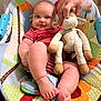 Joel is registered to the contest to win money with this photo: baby, child, infant, onesie, striped_clothing, stuffed_animal, hand, baby_chair, colorful, smiling, happy, cute, toys, indoor, person, legs, feet, plush_toy, comfort, home