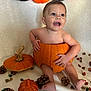 baby, pumpkin, halloween, pine_cones, autumn, decorations, orange, child, smiling, holiday, festive, cute, sitting, face, head, background, celebration, seasonal, indoors, happy