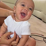 Beau joined the competition — help win amazing prizes! baby, child, infant, smiling, happy, white_clothing, sitting, carpet, living_room, couch, cushion, hand, supporting, indoor, cute, person, face, legs, feet, skin