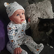 Jordan is registered to the contest to win money with this photo: baby, infant, child, onesie, hat, couch, pillow, cat, pet, indoor, furniture, cute, curious, sitting, soft, cozy, patterned_clothing, wide_eyes, portrait, home