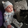 baby, infant, child, onesie, hat, couch, pillow, cat, pet, indoor, furniture, cute, curious, sitting, soft, cozy, patterned_clothing, wide_eyes, portrait, home