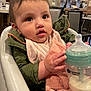 baby, bottle, high_chair, indoor, child, milk, jacket, bib, pink, green, face, hand, table, chair, dining_room, person, cute, infant, feeding, expression