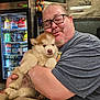 man, glasses, puppy, dog, hugging, countertop, refrigerator, beverage, plush_toy, mario, tattoo, casual_clothing, indoor, smiling, portrait, cute, pet, happy, animal, friendly
