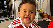 Gia Elora joined the competition — help win amazing prizes! baby, child, smiling, arsenal_jersey, red_and_white_clothing, sock, indoor, living_room, playpen, television, person, furniture, couch, phone, hand, curly_hair, carpet, toy, happy, portrait