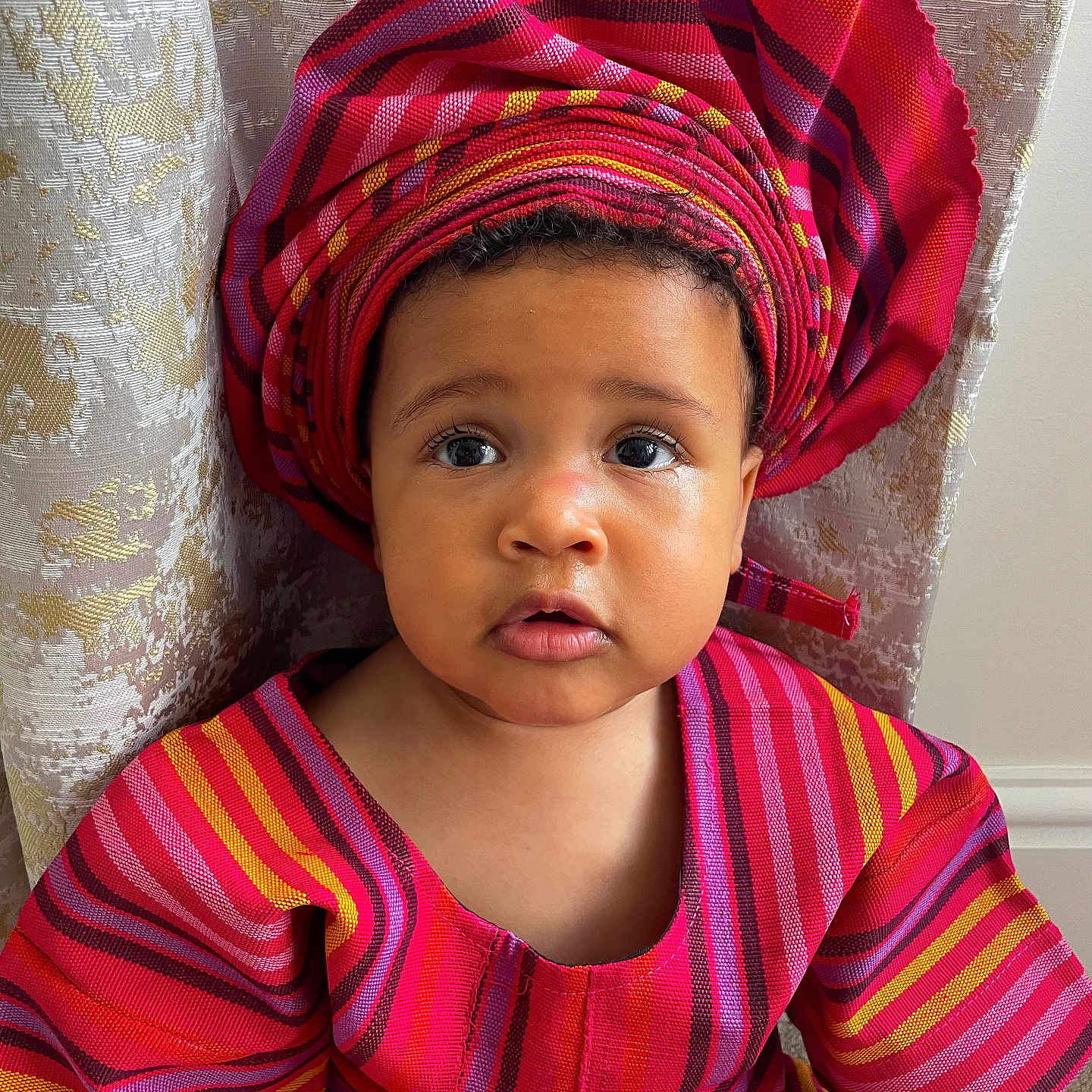 Gia Elora joined the competition — help win amazing prizes! child, toddler, face, headwrap, traditional_clothing, red, pink, striped, curious, indoors, portrait, sitting, fabric, pattern, textile, person, young_child, cute, expression, curtain
