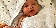 Gia is registered to the contest to win money with this photo: baby, towel, hooded_towel, infant, changing_pad, star_pattern, hand, finger, skin, cute, newborn, wrapped, soft, child, smiling, indoors, person, baby_care, blanket, comfort