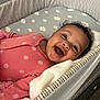 Gia is registered to the contest to win money with this photo: baby, blanket, child, cloud_pattern, cozy, crib, cute, face, happy, head, indoor, infant, mesh, newborn, pink_onesie, polka_dots, portrait, sleeping_area, smiling, striped