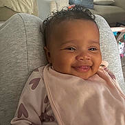 Gia joined the competition — help win amazing prizes! baby, child, clothing, couch, cozy, curly_hair, cute, face, happy, heart_pattern, home, indoor, infant, person, pink_bib, portrait, relaxed, sitting, smiling, toddler