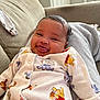 Gia is registered to the contest to win money with this photo: baby, smiling, tongue_out, winnie_the_pooh, onesie, clothing, infant, couch, indoor, happy, face, person, child, cute, cozy, home, soft_light, relaxed, comfort, portrait
