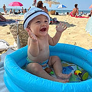 Liam participe au concours pour gagner de l'argent avec cette photo : baby, child, beach, sand, inflatable_pool, water, hat, bucket_hat, smiling, happy, summer, sunny, umbrella, toys, play, vacation, outdoor, sea, people, relax