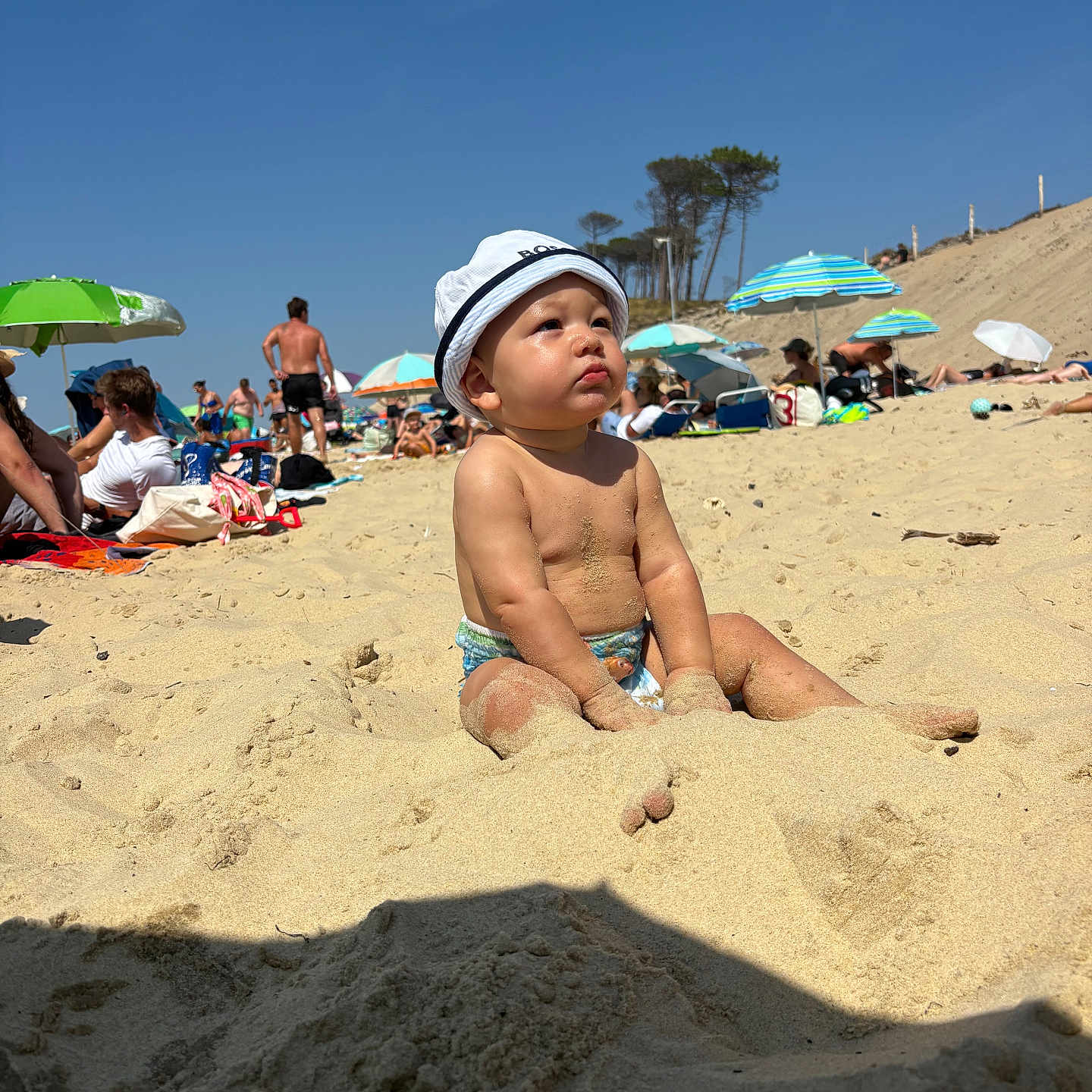 Liam participe au concours pour gagner de l'argent avec cette photo : barefoot, beach, child, daytime, fun, hat, holiday, nature, outdoor, people, portrait, relaxation, sand, sitting, sky, summer, sunny, toddler, umbrella, vacation