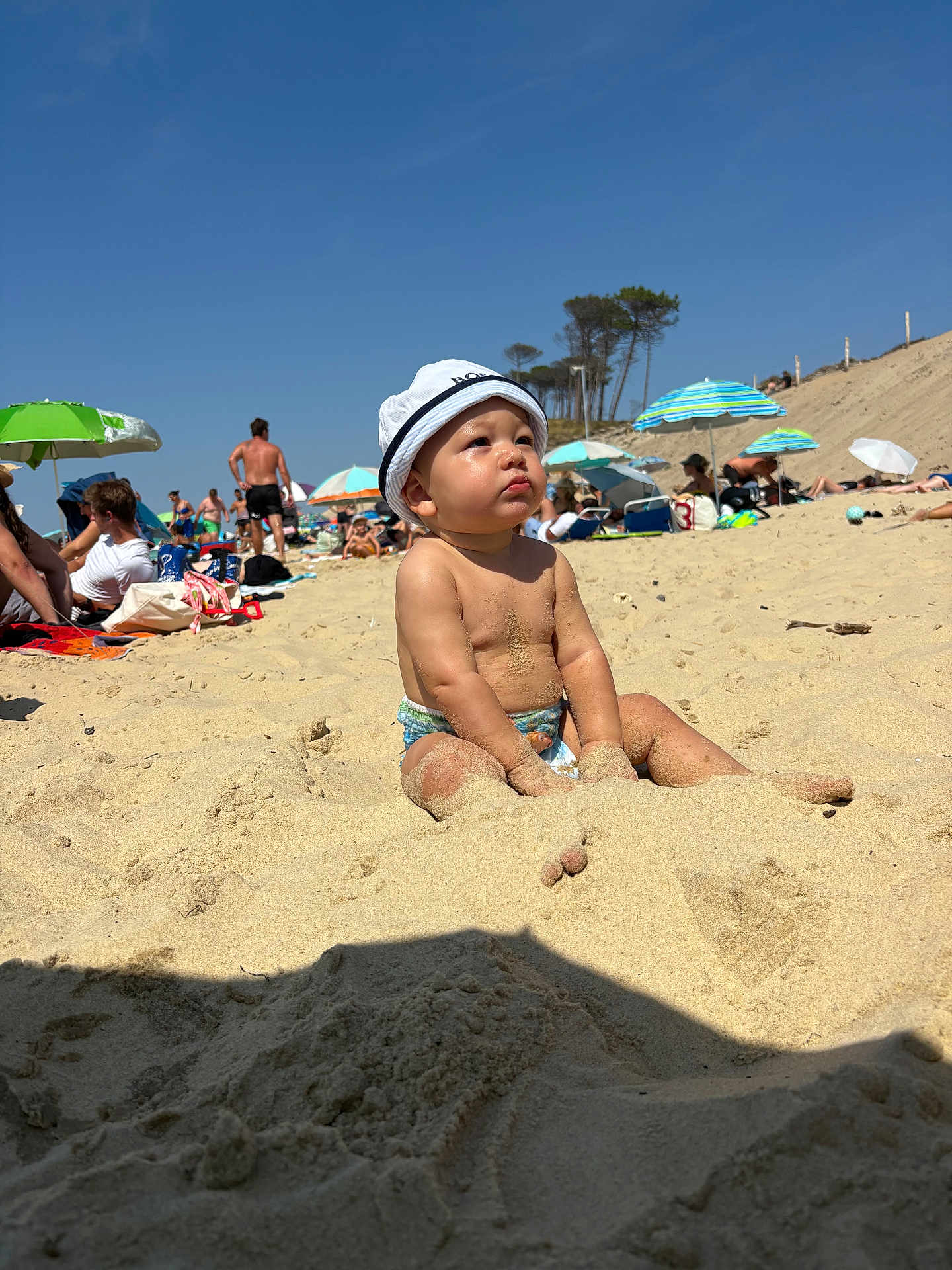 Liam participe au concours pour gagner de l'argent avec cette photo : toddler, child, beach, sand, hat, sunny, summer, umbrella, people, vacation, outdoor, sky, nature, holiday, relaxation, sitting, barefoot, portrait, daytime, fun