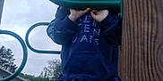Aspen is registered to the contest to win money with this photo: boots, casual_clothing, child, cloudy_sky, curious, daylight, grass, green, handrail, hoodie, nature, outdoor, person, play_structure, playground, residential, shoes, standing, toddler, wood