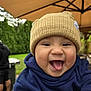 baby, child, hat, knit_hat, hoodie, tongue_out, smiling, outdoor, umbrella, greenery, happy, cute, infant, face, person, apparel, headwear, playful, closeup, daytime