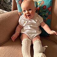 Willow joined the competition — help win amazing prizes! baby, infant, smiling, sitting, floral_pillow, cushion, armchair, white_outfit, knee_socks, bracelet, chubby_legs, cute, portrait, indoor, soft_texture, nursery_decor, wallpaper, happy, legwear, pillowcase