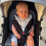 baby, stroller, child, infant, blue_eyes, sitting, outdoor, sunlight, canopy, clothing, straps, safety_buckle, cute, curious, legs, footwear_absent, pavement, summer, portrait, person