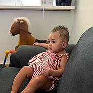 Katalina joined the competition — help win amazing prizes! baby, child, striped_clothing, couch, indoor, plush_toy, rocking_horse, furniture, curly_hair, person, toddler, relaxed, seated, soft_toys, home_interior, casual, infant, cute, living_room, young_child