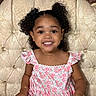 toddler, child, smiling, curly_hair, dress, floral_pattern, pink, lace, chair, tufted, ornate, indoors, portrait, happy, cute, young_child, person, sitting, face, bright