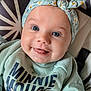 baby, smiling, blue_eyes, headband, floral, clothing, sweatshirt, minnie_mouse, child, cute, portrait, close_up, happy, indoor, cushion, pattern, fabric, person, infant, cozy