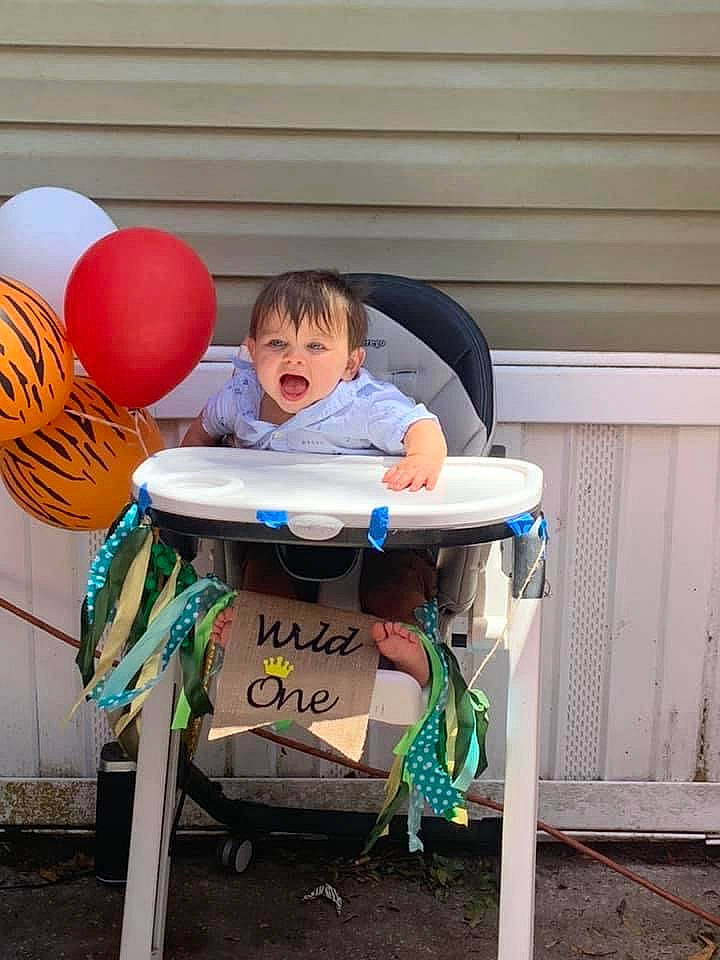 Negan is registered to the contest to win money with this photo: arm, baby, balloon, bench, chair, child, comfort, event, fun, happy, leisure, outdoor_furniture, party_supply, person, play, recreation, sitting, t_shirt, table, toddler